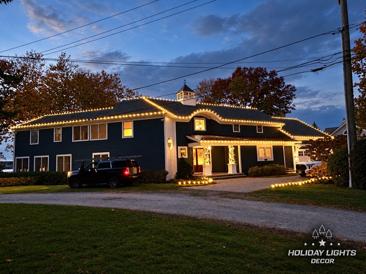 Wide front view of the property with warm white lights outlining the layered rooflines, curved dormer, porch, and driveway borders.