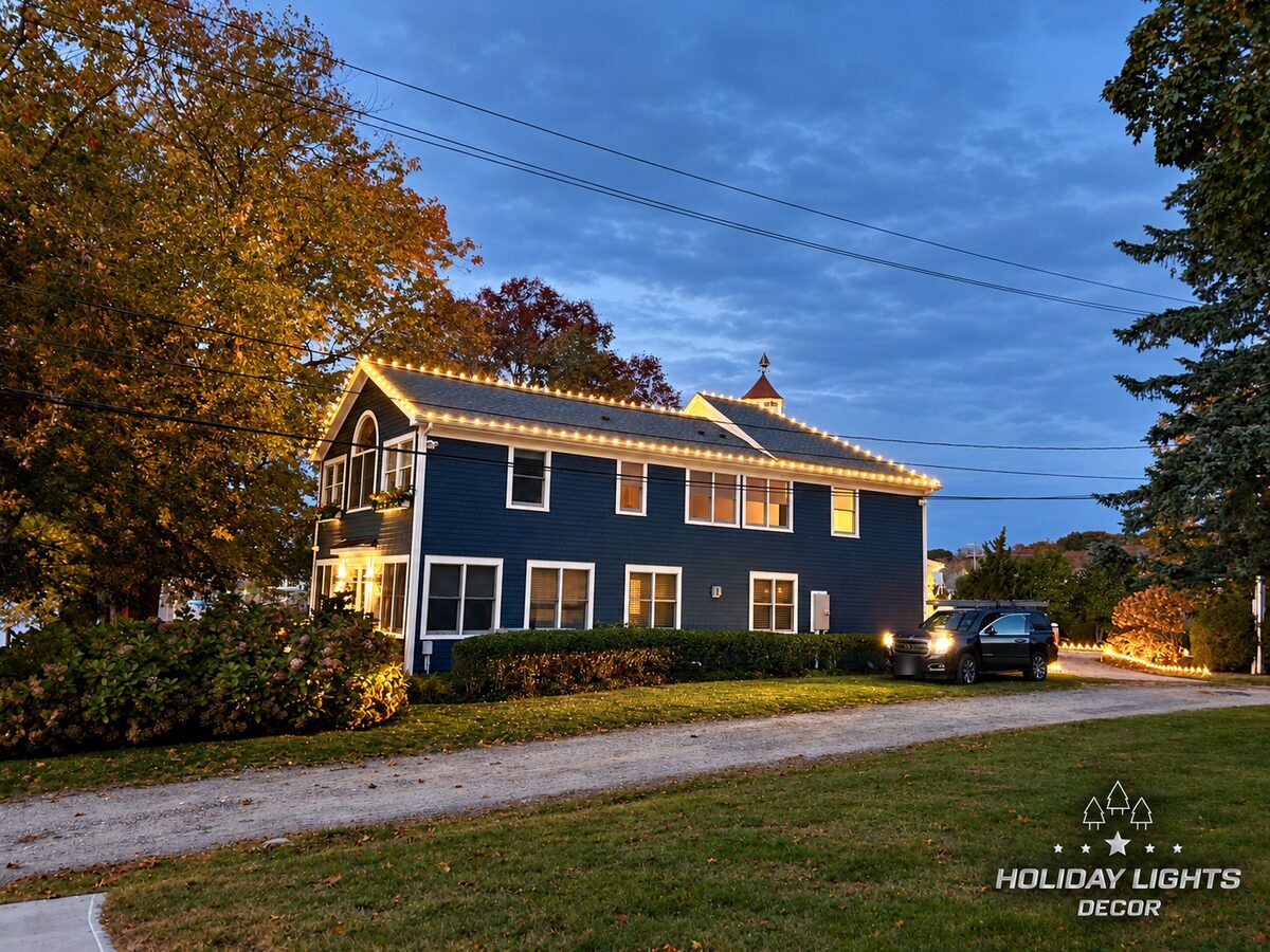 Golden-hour side view showing warm white lights along the upper roof ridge and lower eaves, with additional lighting following the driveway landscaping.